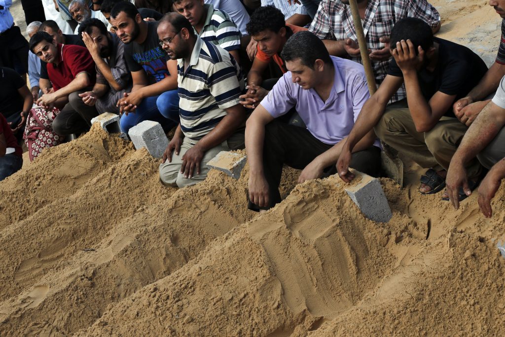 Mourners pray over the fresh graves of members of the Abu Jarad family who were killed in an Israeli strike on their family house, following their funerals in Beit Lahiya, in the northern Gaza Strip, Saturday, July 19, 2014. Eight members of the family were killed Friday night as a result of Israeli tank shelling on their home. Gaza Health Ministry spokesman Ashraf al-Kidra said the new round of strikes raised the death toll from the 12-day offensive to more than 330 Palestinians, many of them civilians. (AP Photo/Lefteris Pitarakis)
