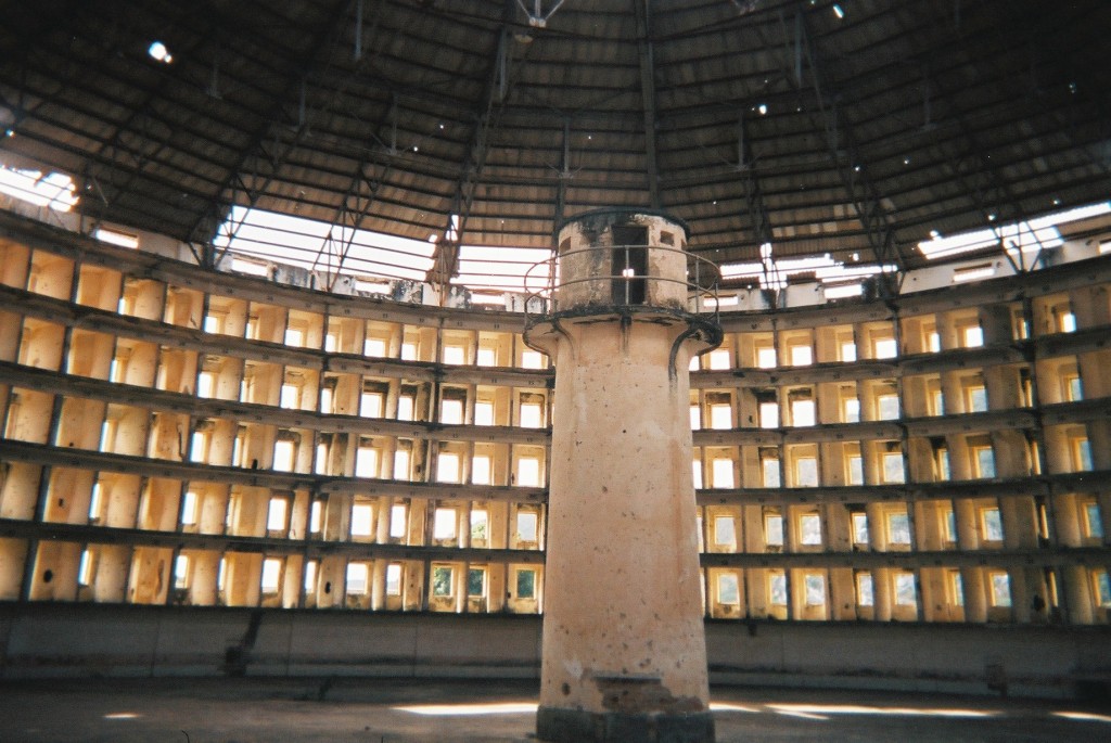 The Panopticon is a type of institutional building designed by the English philosopher and social theorist Jeremy Bentham in the late 18th century.  the concept of the design is to allow a single watchman to observe (-opticon) all (pan-) inmates of an institution without the inmates being able to tell whether or not they are being watched."  Source wikipedia